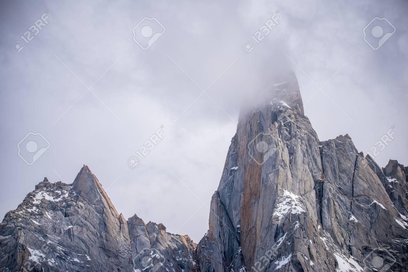 The cloud envelops the top of the rocks. The snow lies on the ledges of the rocks. Sunlight reflects on the rocks. - 107212963 The cloud envelops the top of the rocks. The snow lies on the ledges of the rocks. Sunlight reflects on the rocks. - 107212963