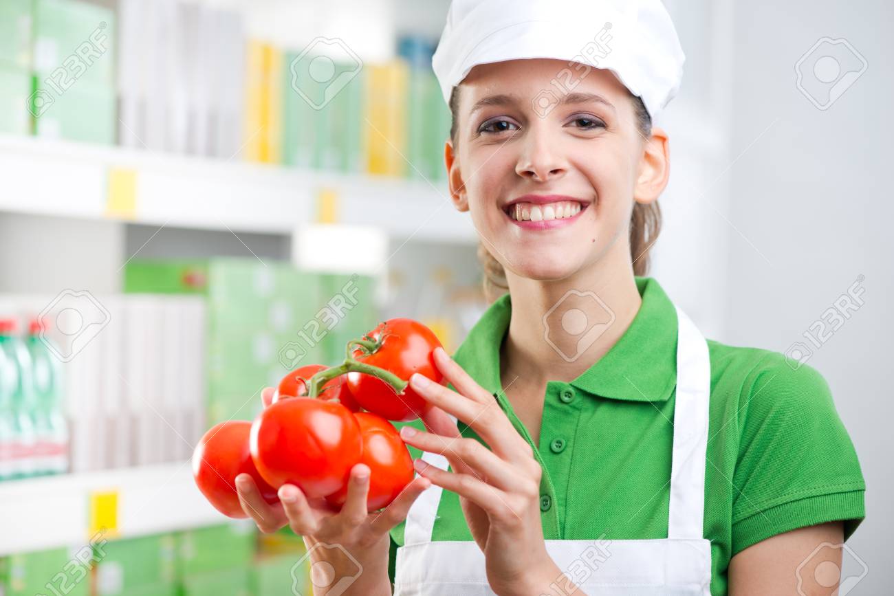 young female sales clerk smiling and holding fresh tomatoes at sales clerk