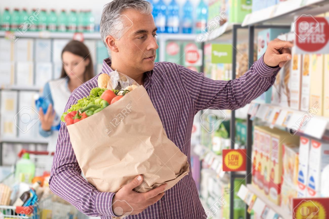 El hombre que hace las compras de comestibles en el supermercado, él está buscando productos en el estante de la tienda y la celebración de una bolsa El hombre que hace las compras de comestibles en el supermercado, él está buscando productos en el estante de la tienda y la celebración de una bolsa