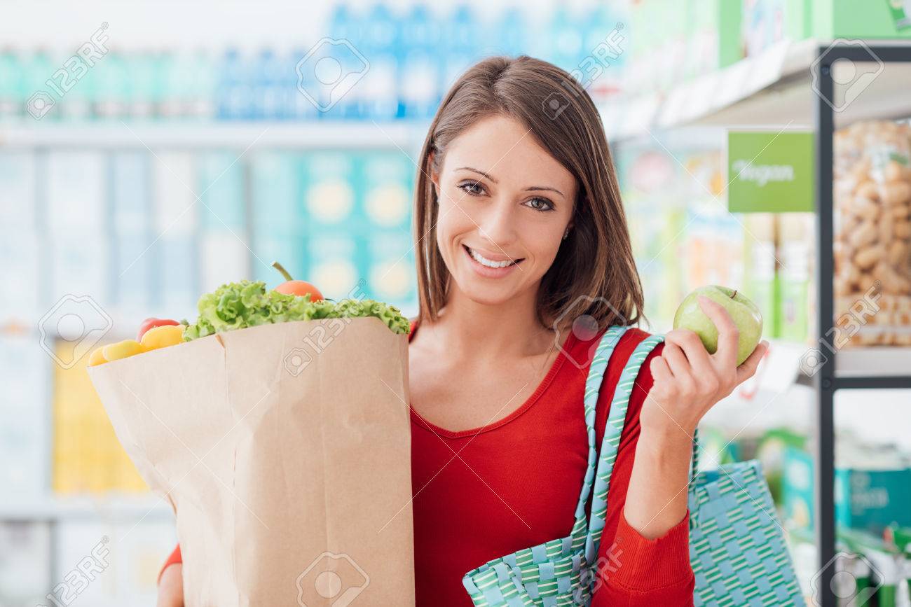 Sonriente mujer joven de compras en el supermercado, ella está sosteniendo una bolsa de supermercado con verduras orgánicas frescas Sonriente mujer joven de compras en el supermercado, ella está sosteniendo una bolsa de supermercado con verduras orgánicas frescas