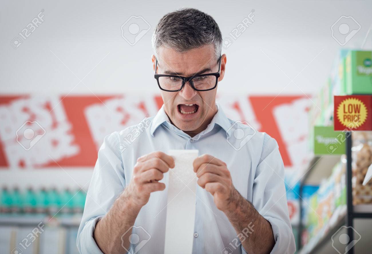 Shocked man doing grocery shopping at the supermarket and checking a long receipt, lifestyle and budgeting concept - 68483740 Shocked man doing grocery shopping at the supermarket and checking a long receipt, lifestyle and budgeting concept - 68483740