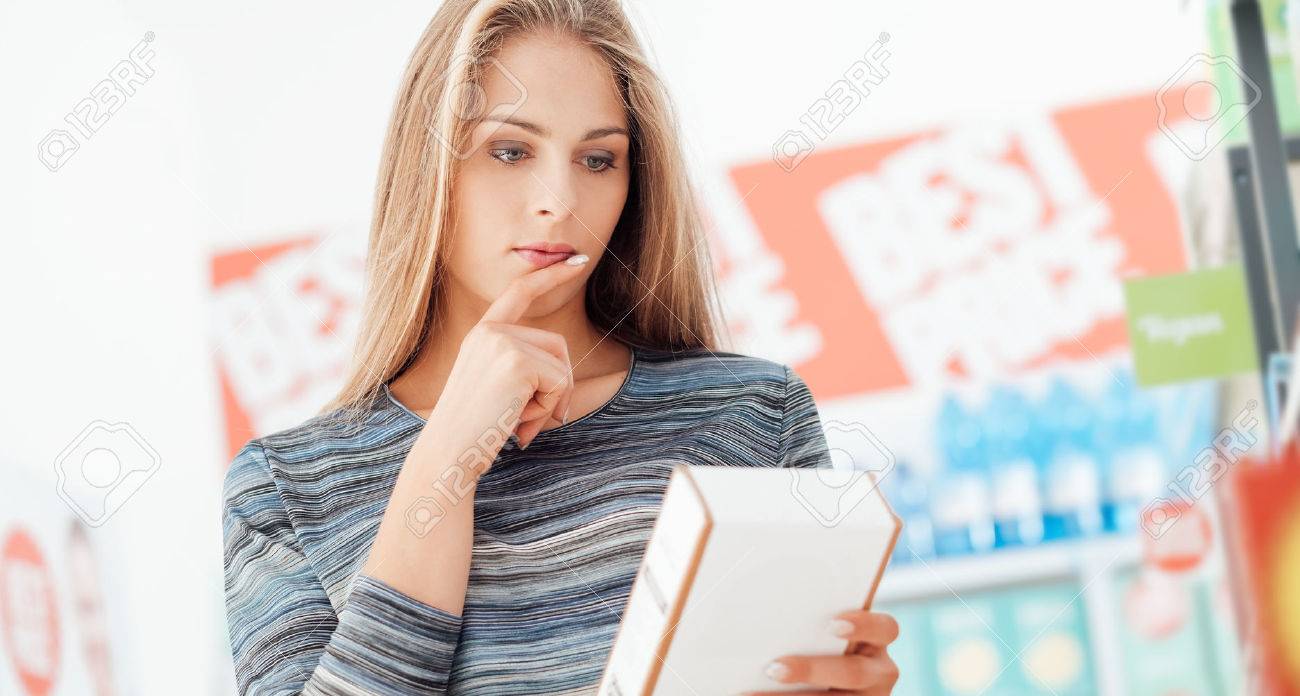Young woman doing grocery shopping at the supermarket and reading a food label with ingredients on a box, shopping and nutrition concept - 67234127 Young woman doing grocery shopping at the supermarket and reading a food label with ingredients on a box, shopping and nutrition concept - 67234127