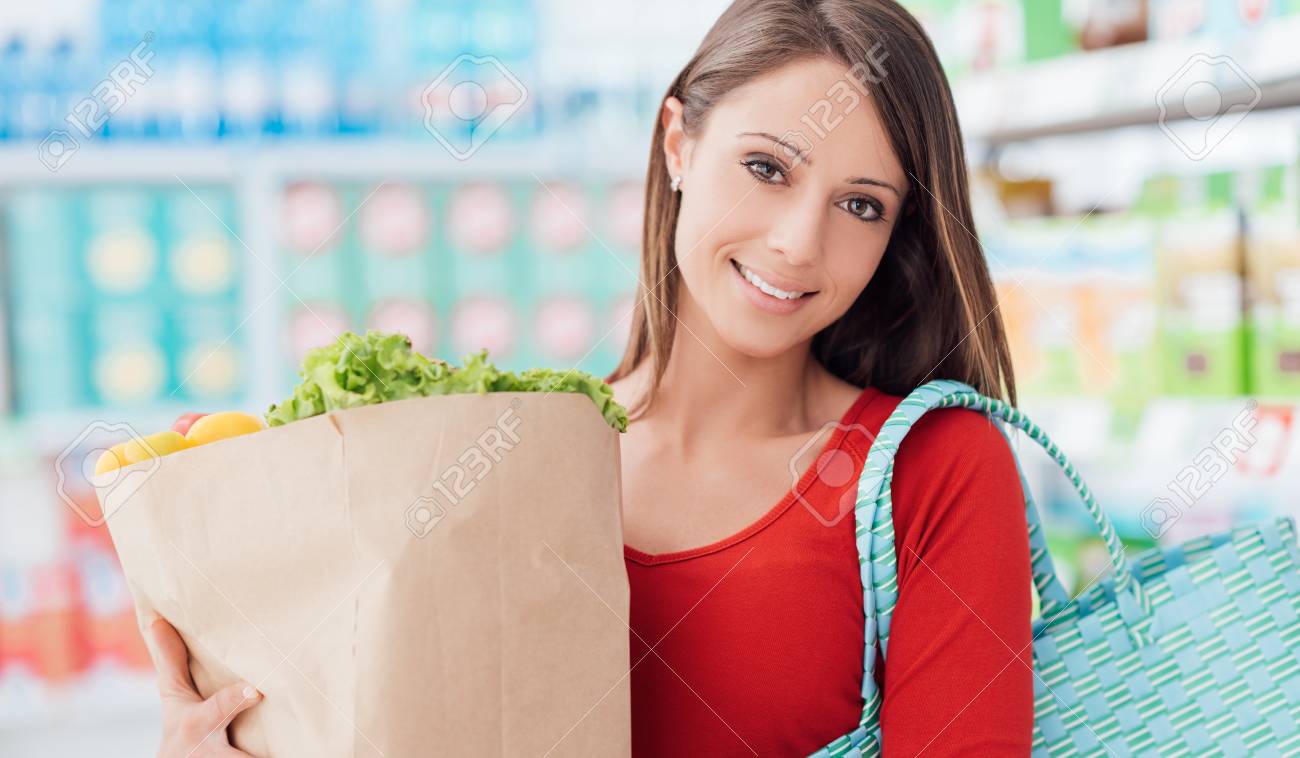Sonriente mujer joven de compras en el supermercado, ella está sosteniendo una bolsa de supermercado con verduras orgánicas frescas Sonriente mujer joven de compras en el supermercado, ella está sosteniendo una bolsa de supermercado con verduras orgánicas frescas