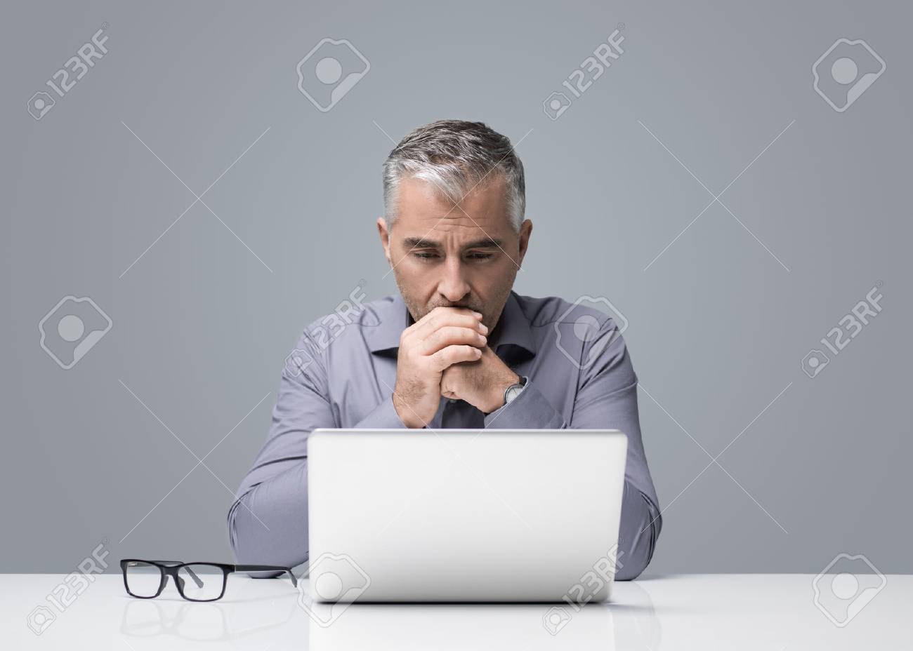 Mature businessman sitting at desk and working with a laptop, he is reading and thinking, business strategies and problem solving concept - 91424987 Mature businessman sitting at desk and working with a laptop, he is reading and thinking, business strategies and problem solving concept - 91424987