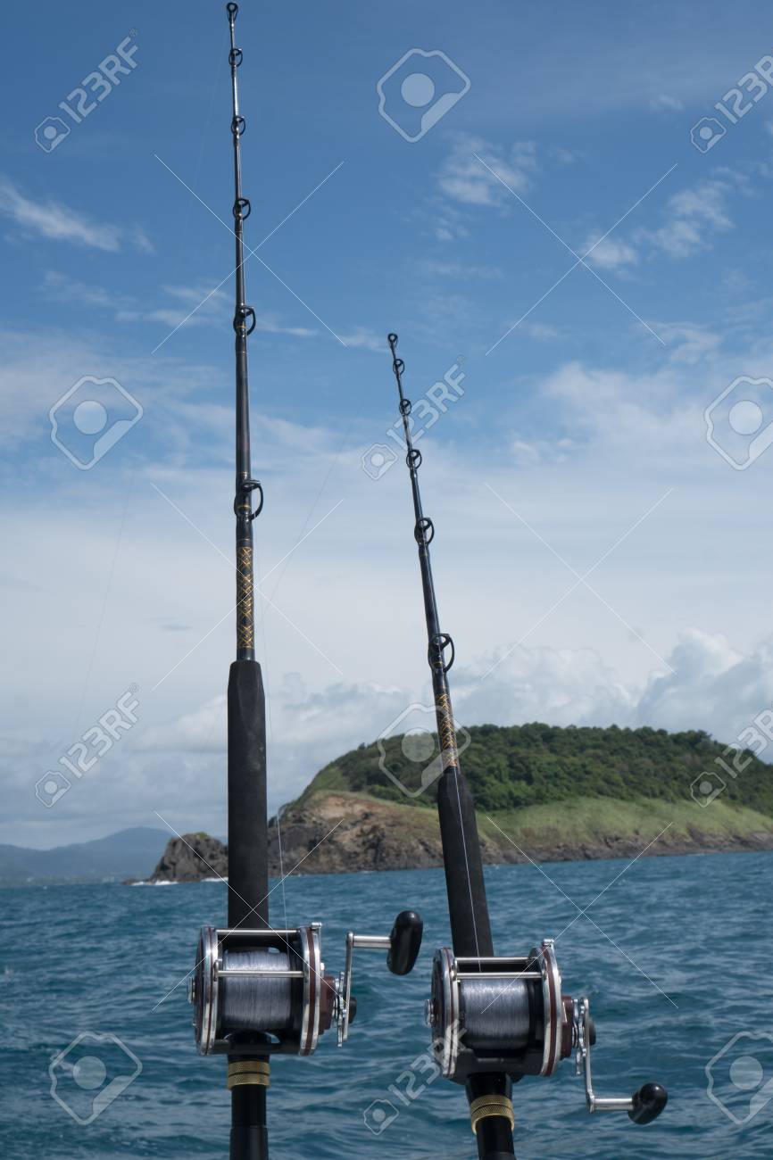 Cañas De Pescar En Un Barco Sobre El Mar Azul, Cielo Y Isla Verde. Fotografía De Cañas De Pescar En Sostenedores Del Poste En La Parte Posterior De Un Barco
