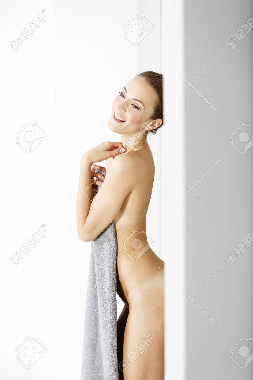 Attractive woman leaning against a wall with a towel draped over her getting dressed - 44209974