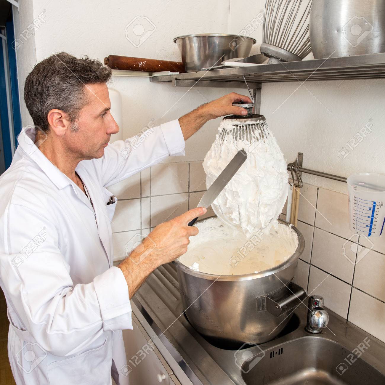 middle aged male professional cook cleaning a big whisk from stock