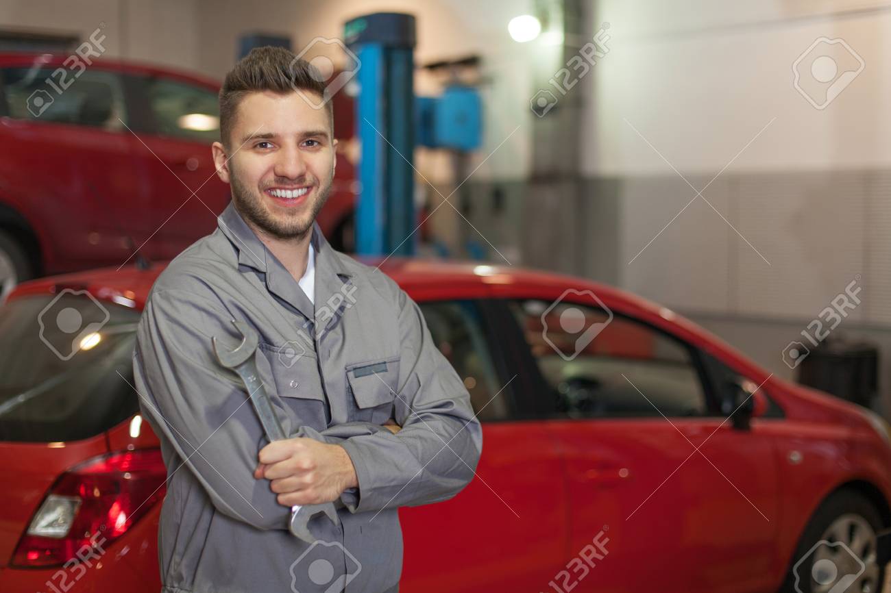 作業服ワーク ショップの 2 つの赤い車に対してレンチとポーズで笑みを浮かべて男 の写真素材 画像素材 Image