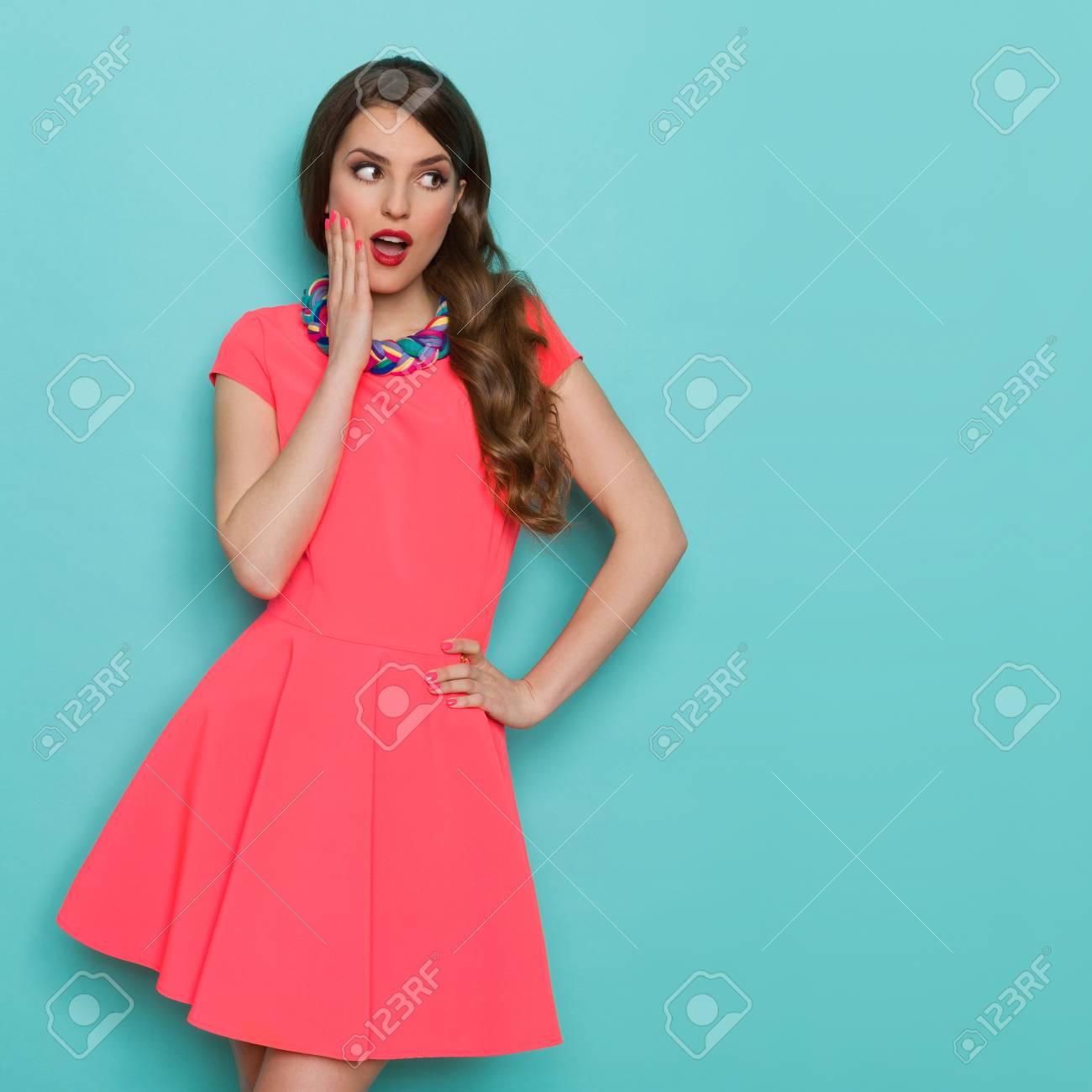 ピンクのミニドレスのあごに手でポーズとよそ見で美しい若い女性は驚いた 4 分の 3 の長さスタジオは 背景色が水色の撮影 の写真素材 画像素材 Image