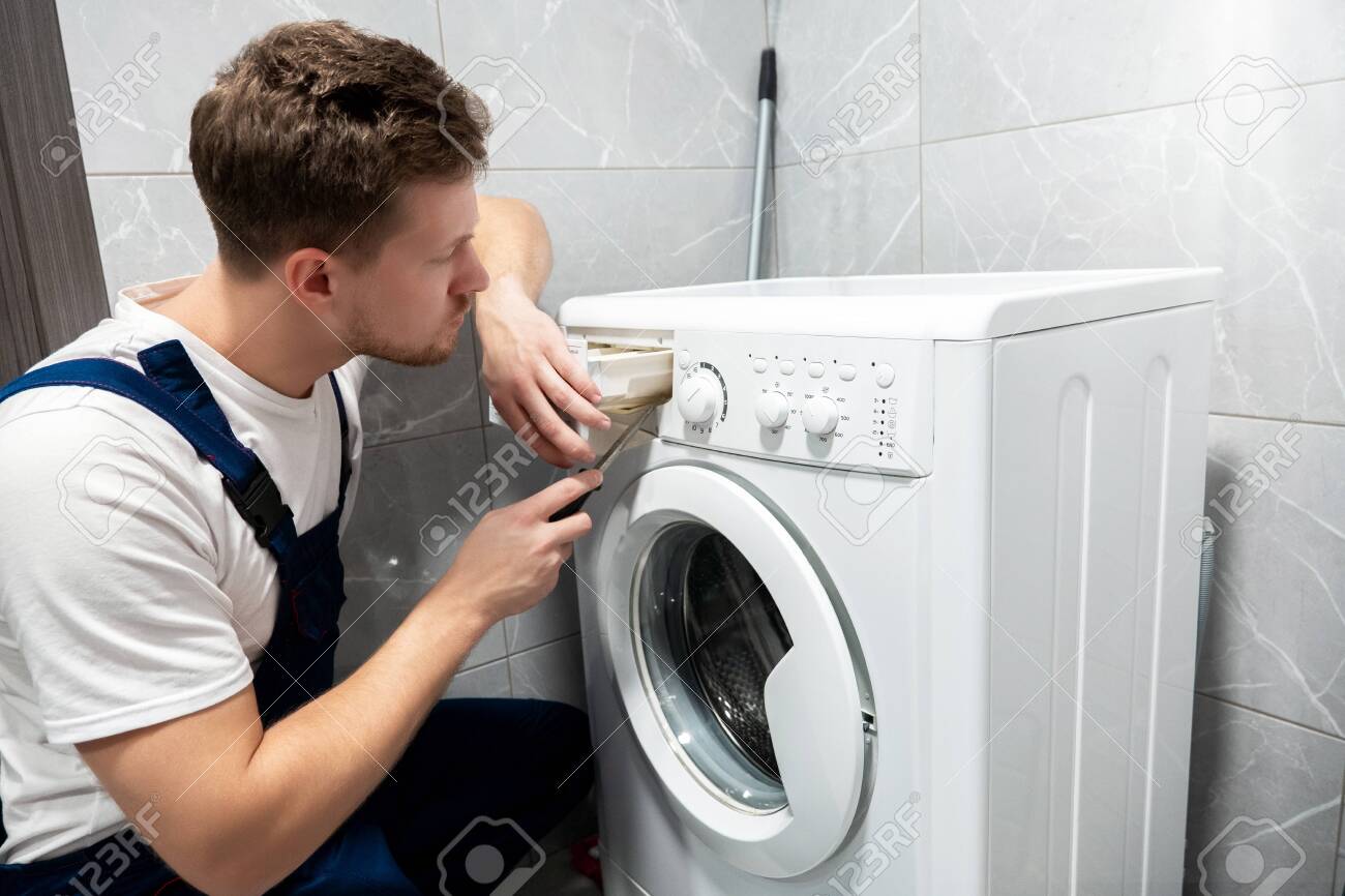 young handsome man worker in uniform repairing washing machine at home in the toilette professional repair service - 137642234 young handsome man worker in uniform repairing washing machine at home in the toilette professional repair service - 137642234