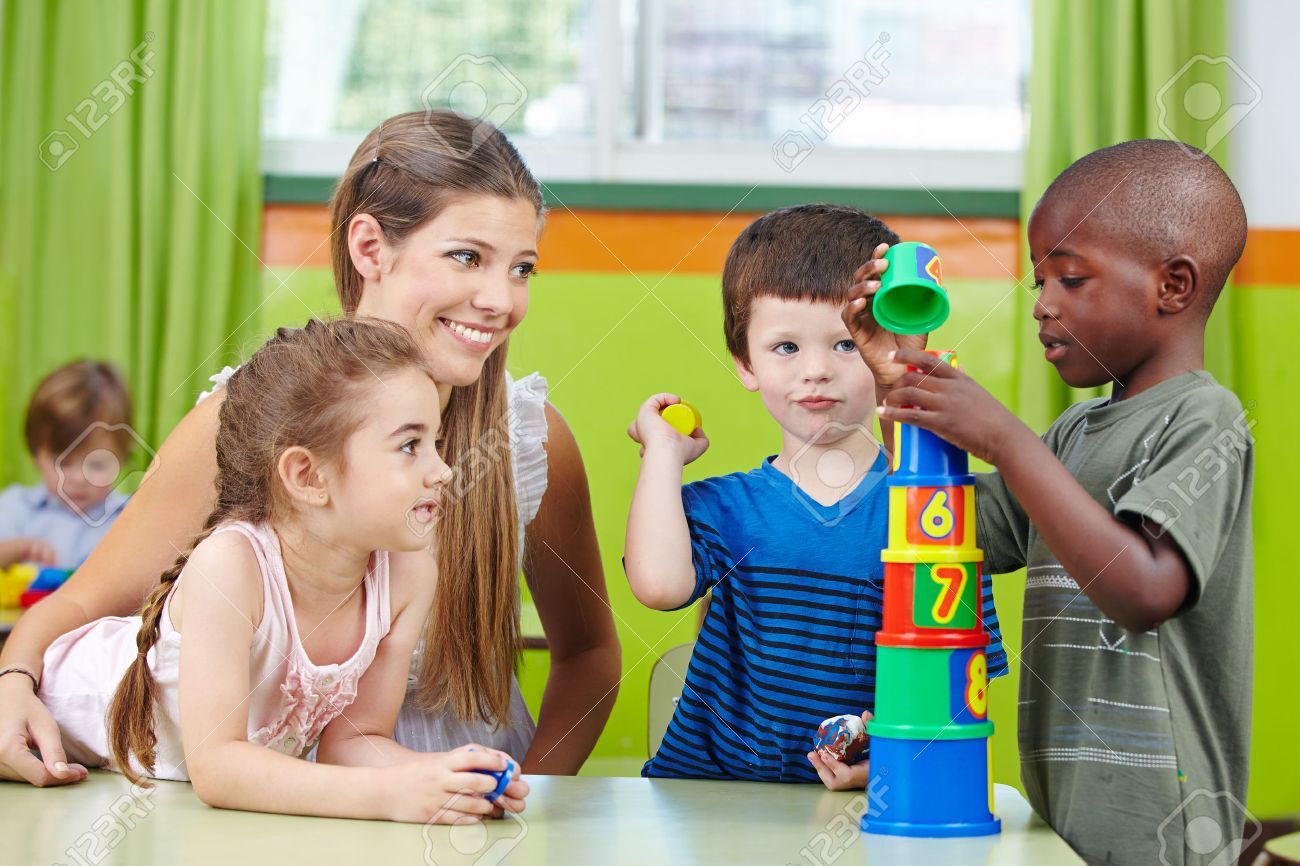 children with nursery teacher building tower in a kindergarten nursery teacher