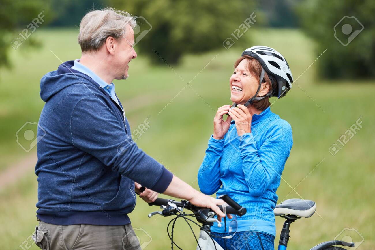 Active senior woman puts on a bicycle helmet with partner before the bike ride - 121179148 Active senior woman puts on a bicycle helmet with partner before the bike ride - 121179148