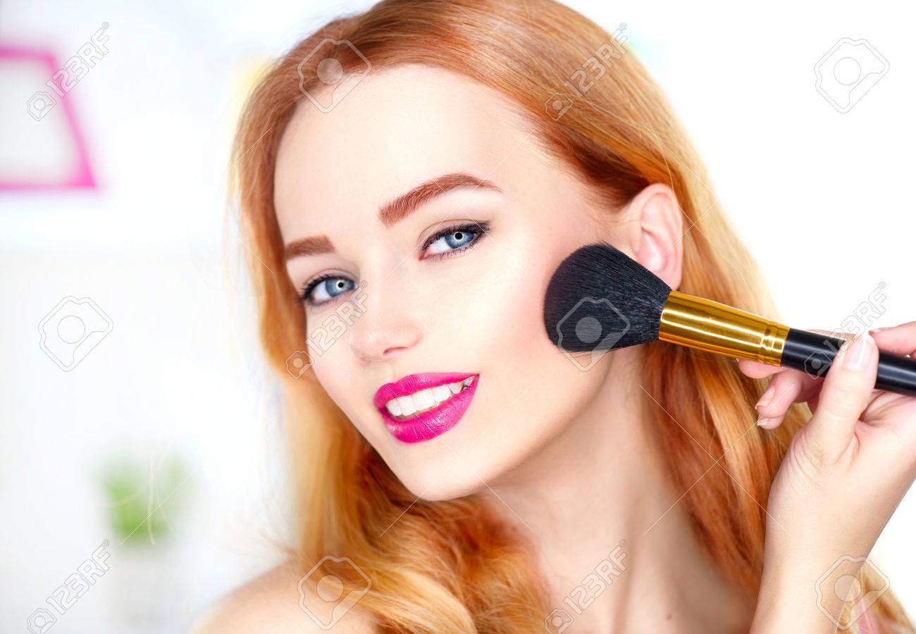 Beauty woman applying makeup. Beautiful girl looking in the mirror and applying cosmetic with a big brush - 75720341 Beauty woman applying makeup. Beautiful girl looking in the mirror and applying cosmetic with a big brush - 75720341