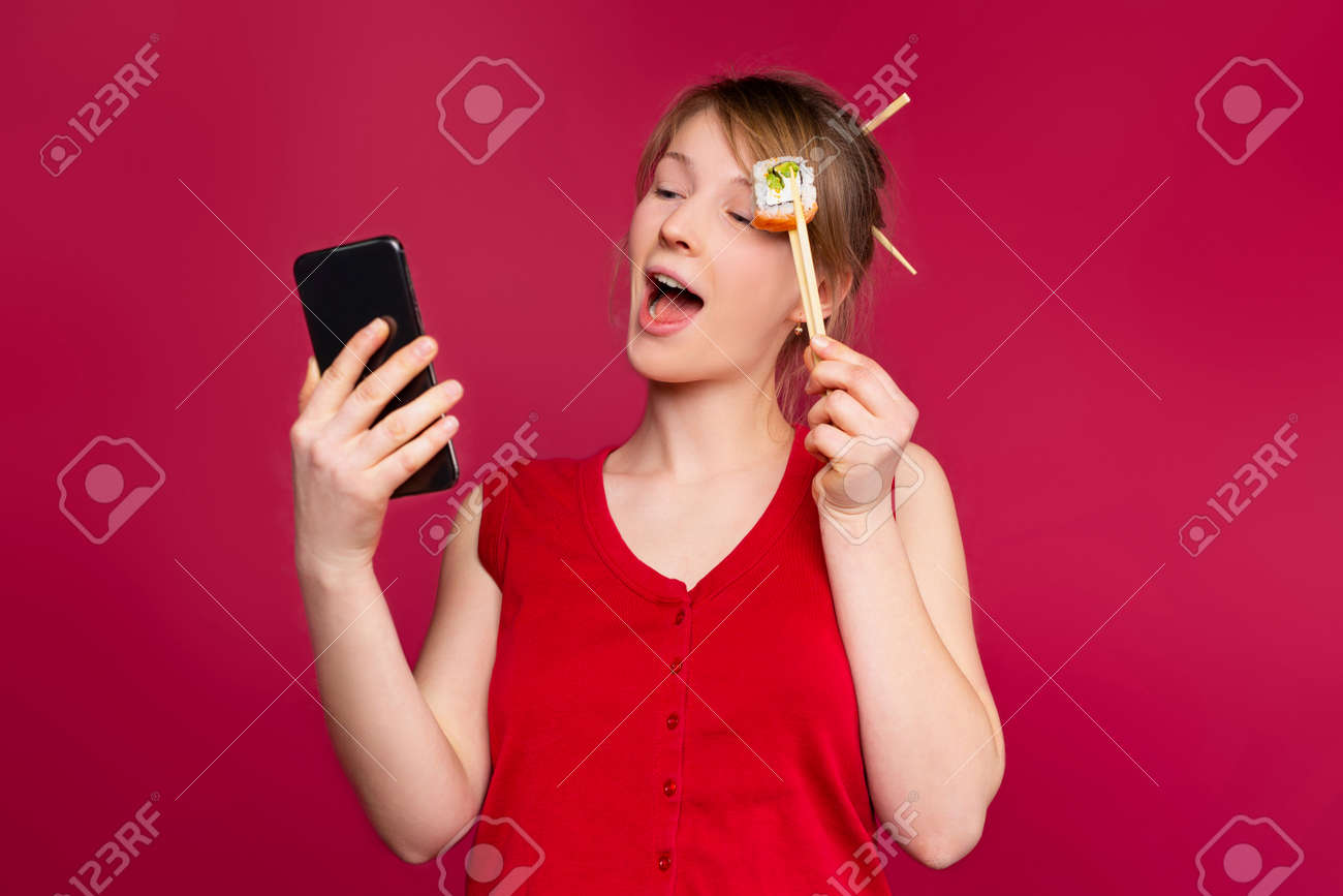 電話で話している若い女の子、ライブチャット、ストリームフードブロガー。スマートフォンで注文する白人の女の子、寿司の役割に重点を置くの写真素材・画像素材  Image 165398170