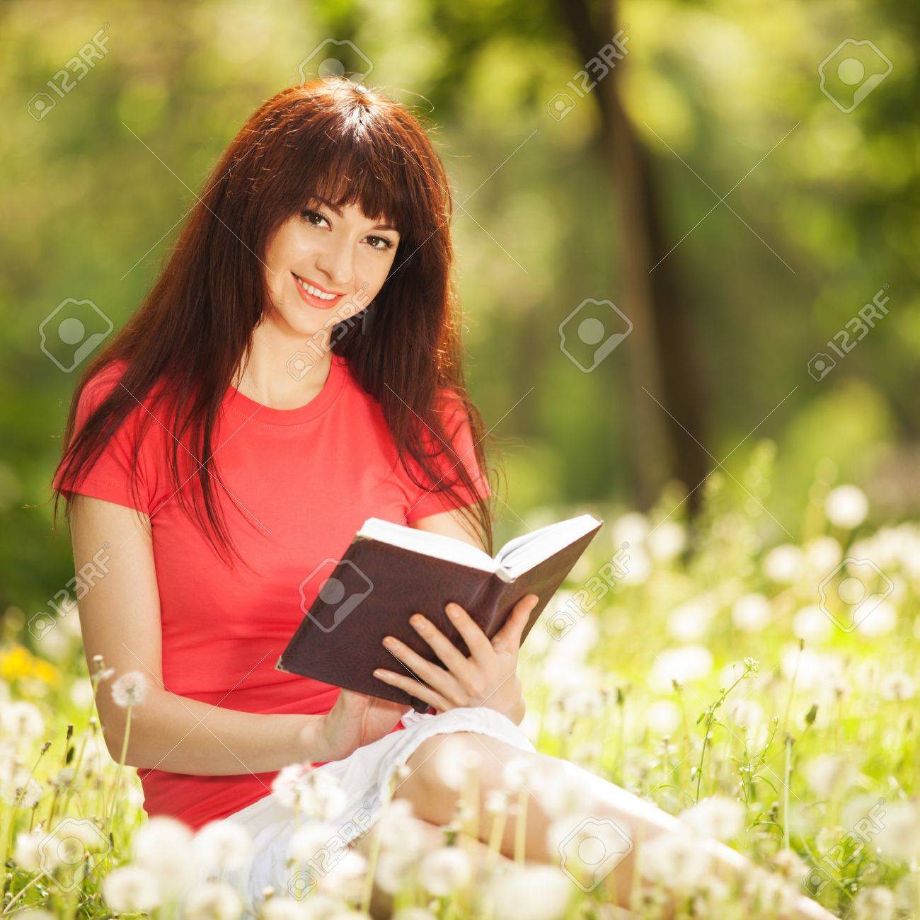 young woman reading a book in the park with flowers stock photo