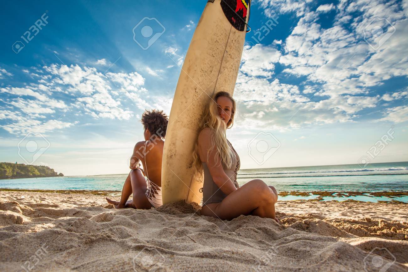 Meninas De Surfista De Casal De Raca Mista Sentadas De Costas Para Tras Com A Prancha No Meio Da Frente De Uma Paisagem Marinha De Tirar O Folego Observando Ondas Na Praia