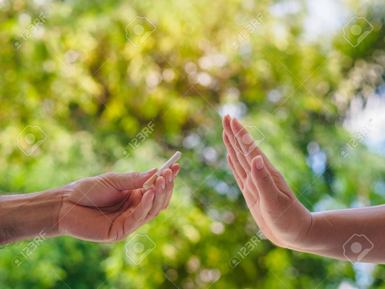 No smoking. Close up of male hands holding cigarettes and proposing it to person. The human arm is gesturing with refusal on bokeh background. - 101809914 No smoking. Close up of male hands holding cigarettes and proposing it to person. The human arm is gesturing with refusal on bokeh background. - 101809914