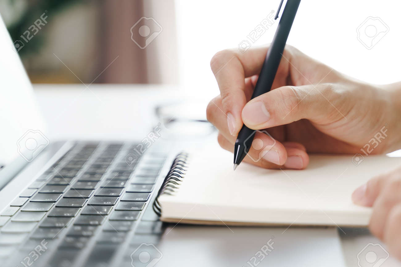 Close up of young man in casual cloth hands writing down on the notepad, notebook using ballpoint pen with laptop computer on the table. - 171856036 Close up of young man in casual cloth hands writing down on the notepad, notebook using ballpoint pen with laptop computer on the table. - 171856036