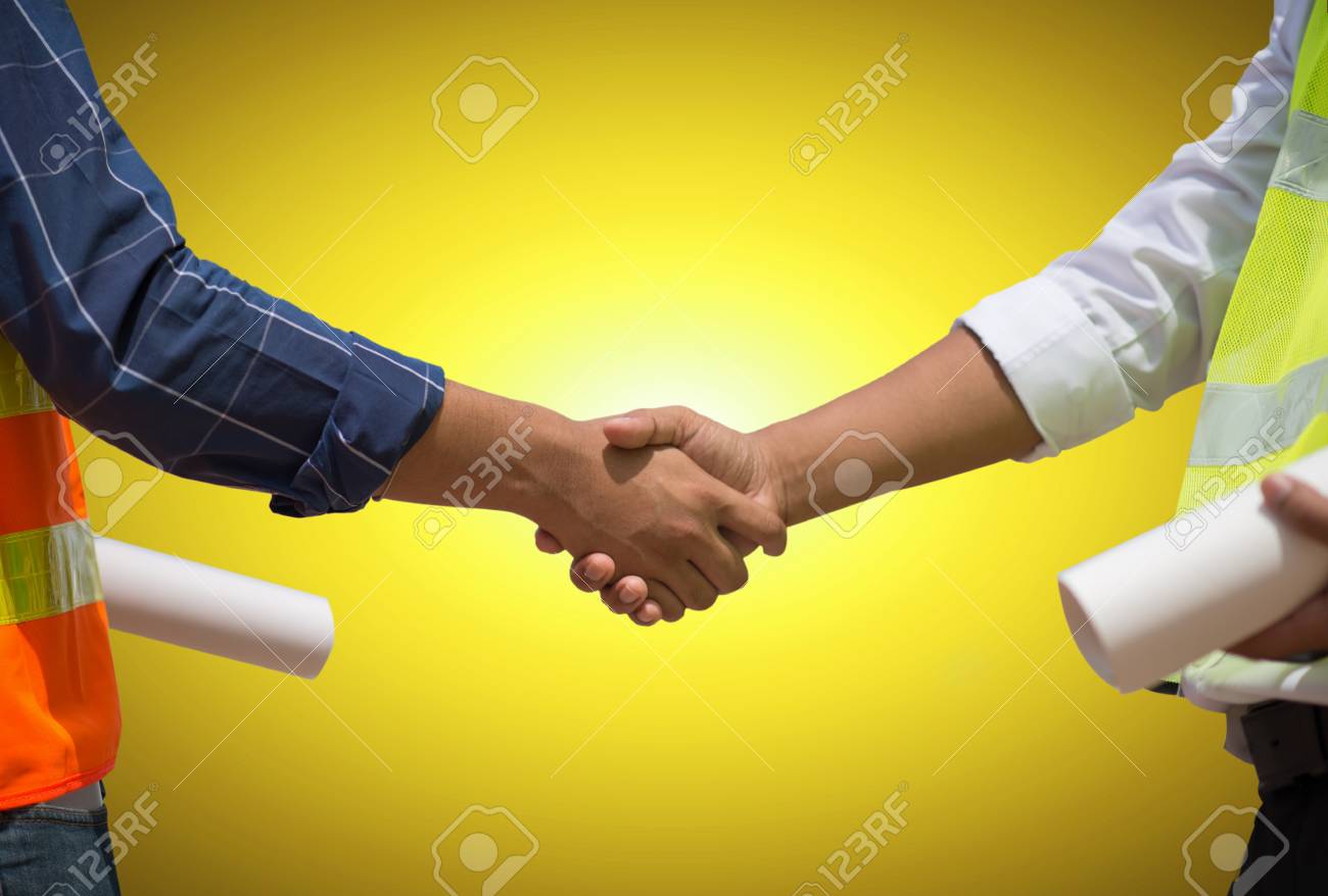 Handsome construction workers in protective helmets and vests are shaking hands while working in the office center, Horizontal, Blurred background - 104430270 Handsome construction workers in protective helmets and vests are shaking hands while working in the office center, Horizontal, Blurred background - 104430270