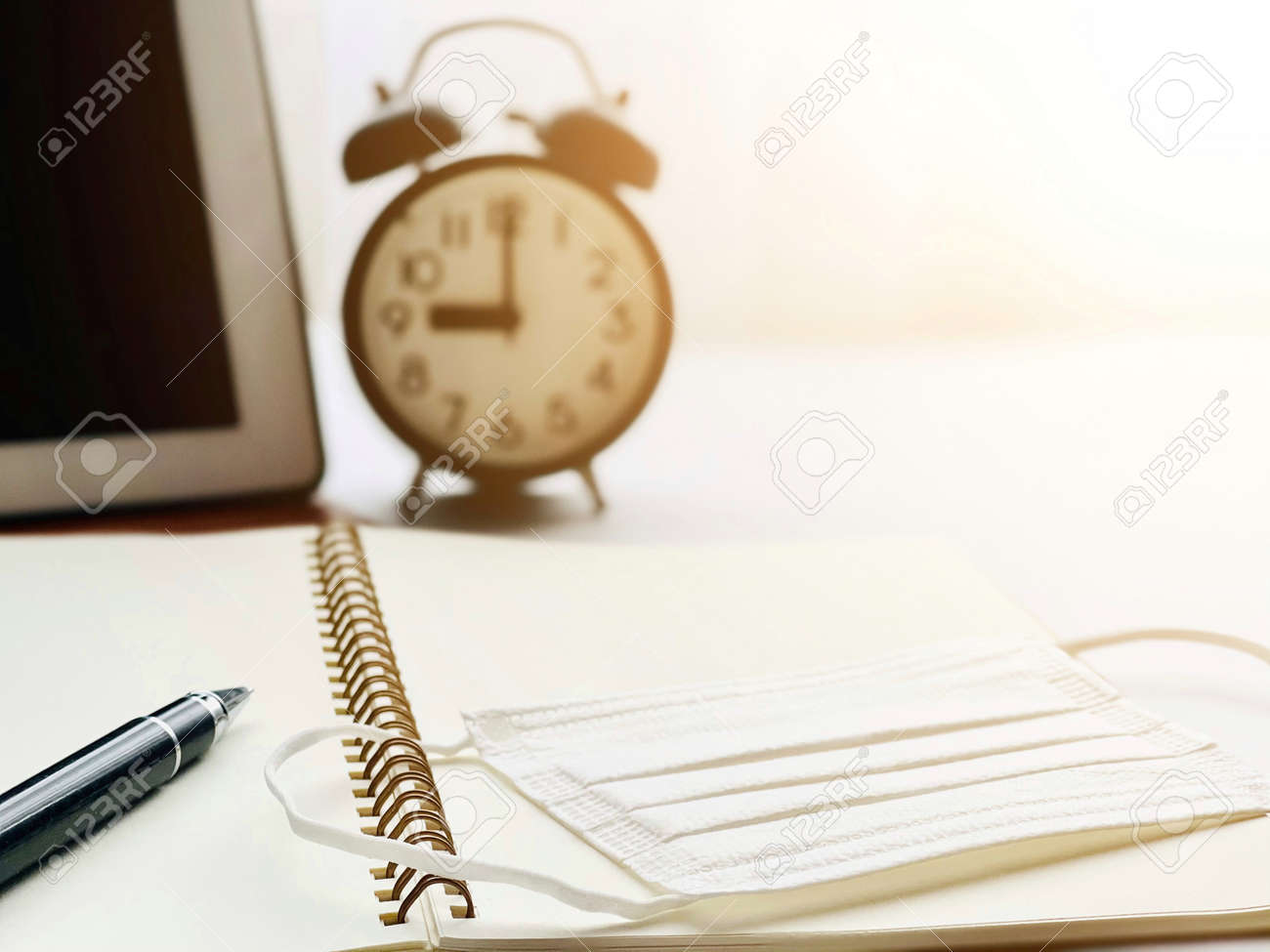 Anti virus protection mask on open notebook paper, digital tablet and clock on working desk table - 168796800 Anti virus protection mask on open notebook paper, digital tablet and clock on working desk table - 168796800
