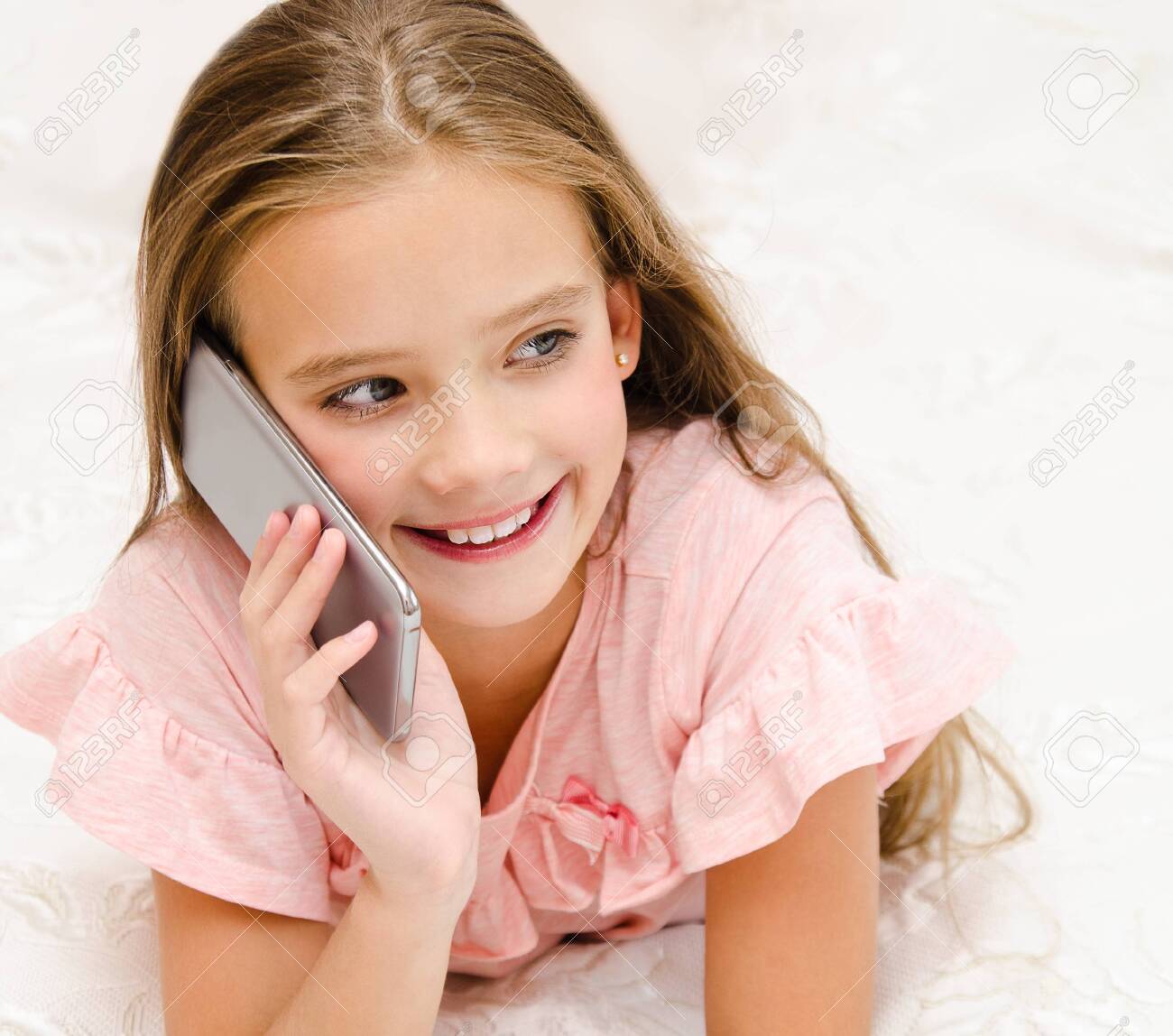 Portrait Of Cute Smiling Little Girl Child Calling By Cell Phone Smartphone Lying On The Bed At Home Stock Photo, Picture And Royalty Free Image. Image 129270179.