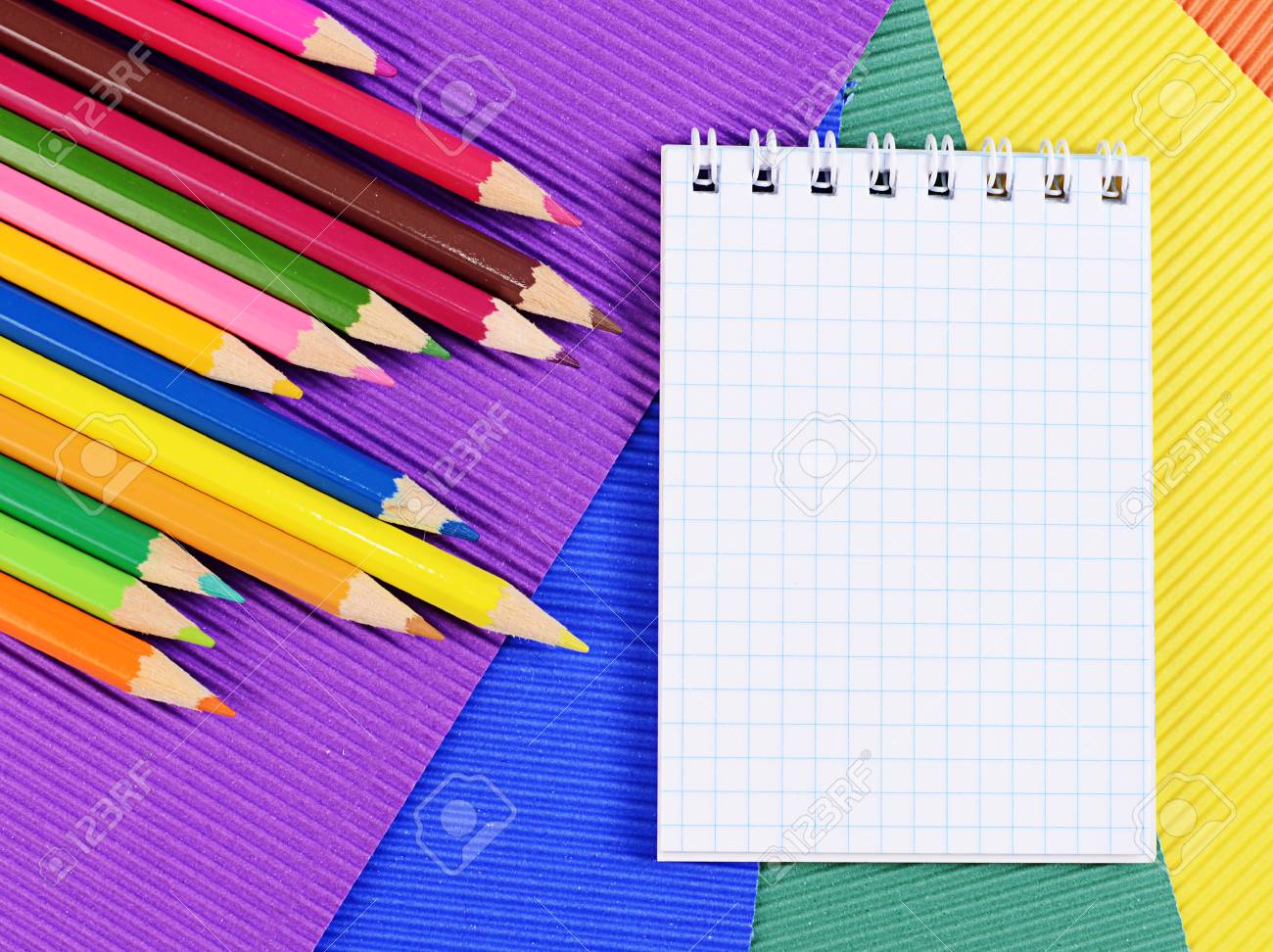 color pencils on multi colored paper with notebook stock photo