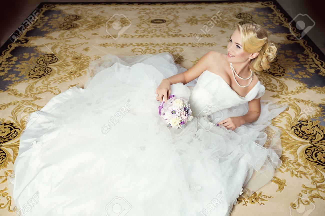カーペットの上に横たわって白のふわふわドレスで美しい若い花嫁 の 