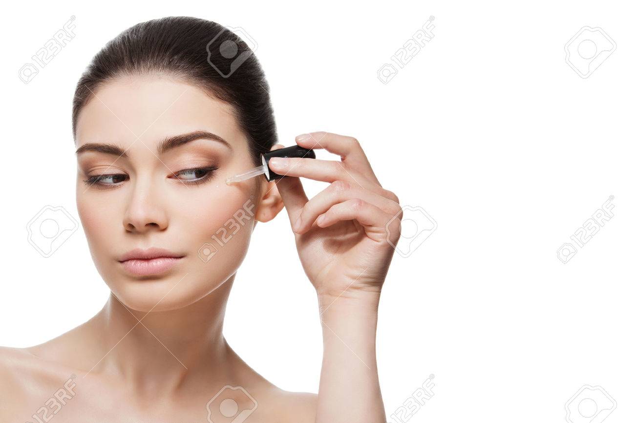 Beautiful young woman applying anti-ageing moisturizing serum to under eye area. Isolated over white background. Copy space. - 44387741 Beautiful young woman applying anti-ageing moisturizing serum to under eye area. Isolated over white background. Copy space. - 44387741