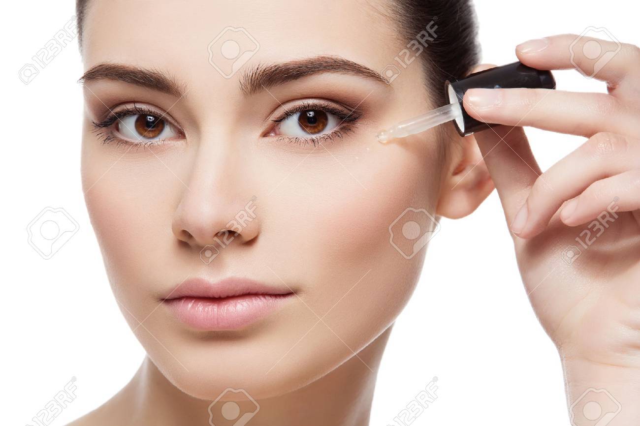 Beautiful young woman applying serum moisturizer on under eye area. Beauty shot. Close-up. Isolated over white background. - 52484745 Beautiful young woman applying serum moisturizer on under eye area. Beauty shot. Close-up. Isolated over white background. - 52484745
