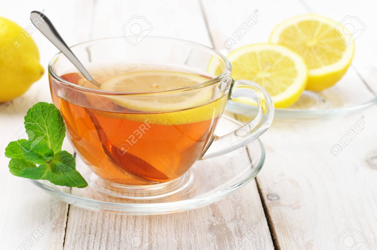Tè Fresco Con Limone E Menta In Tazza Di Vetro E Tagliare Il Limone Sul Rustico Tavolo In Legno Bianco Malandato