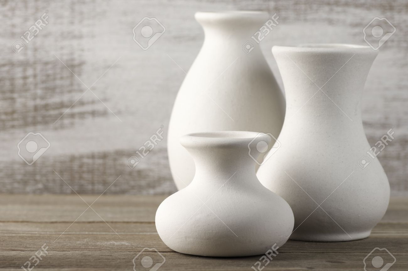 Three Empty White Unglazed Ceramic Vases On Wooden Table Against