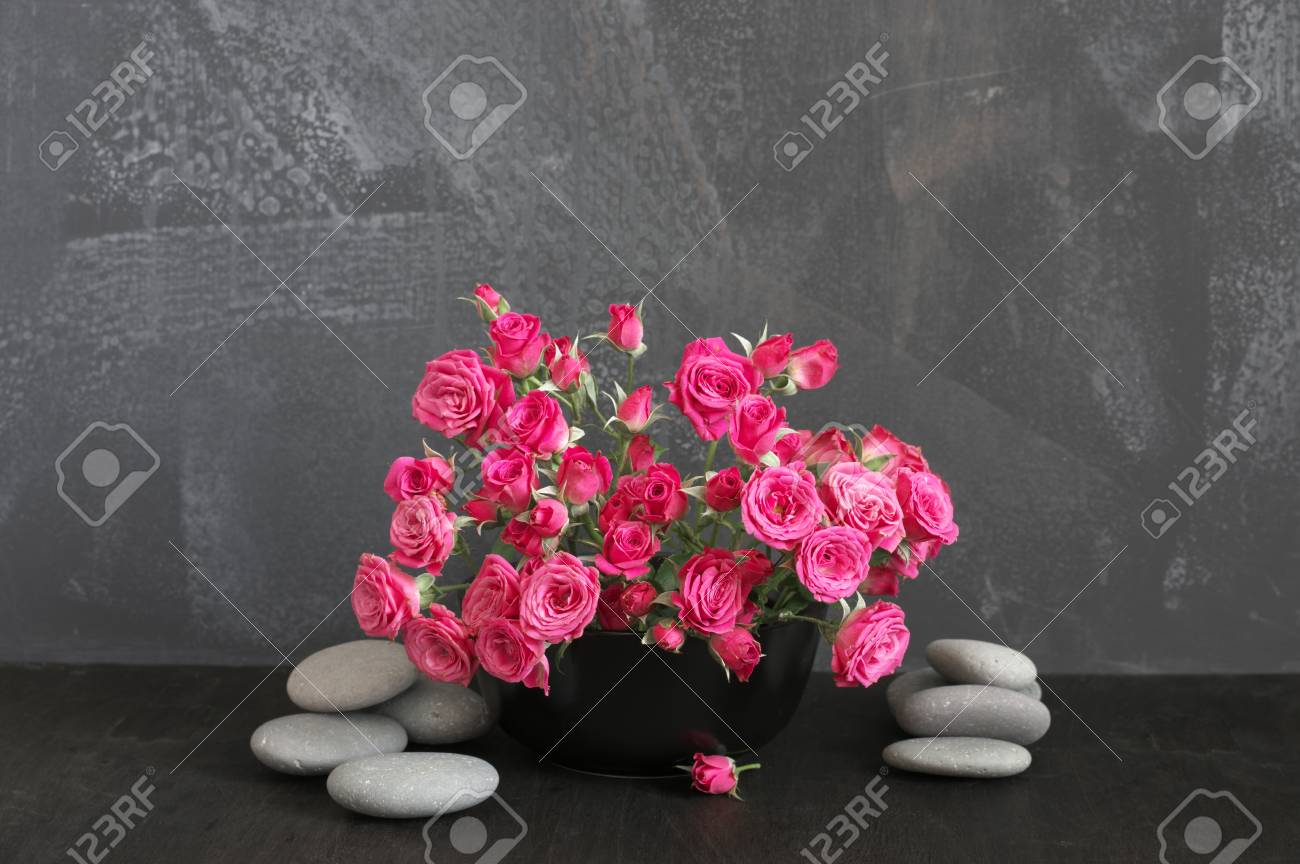Bouquet of crimson spray roses in black vase and pebble on black..