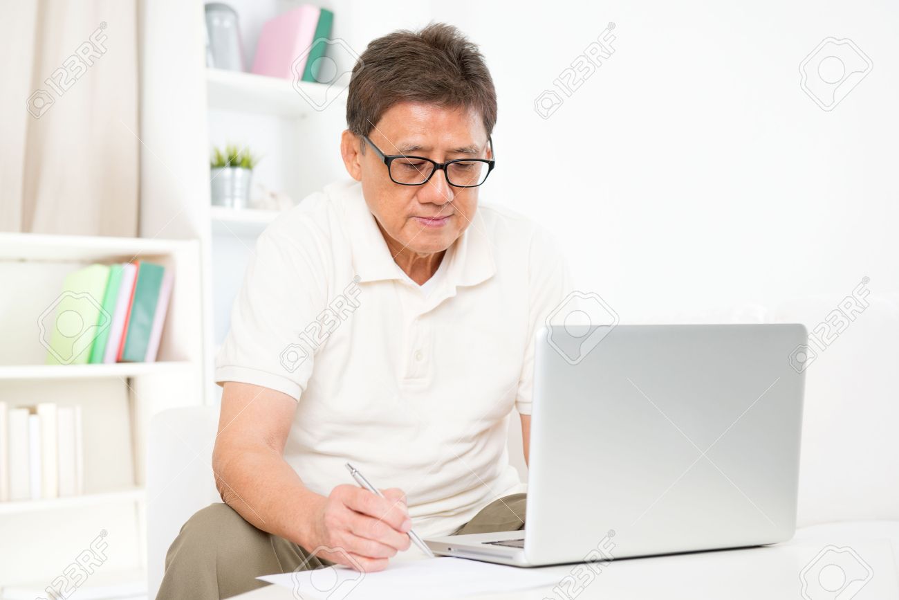 Portrait of mature Asian man using computer laptop and writing something on paper, sitting on sofa at home, senior retiree indoors living lifestyle. - 33193650 Portrait of mature Asian man using computer laptop and writing something on paper, sitting on sofa at home, senior retiree indoors living lifestyle. - 33193650