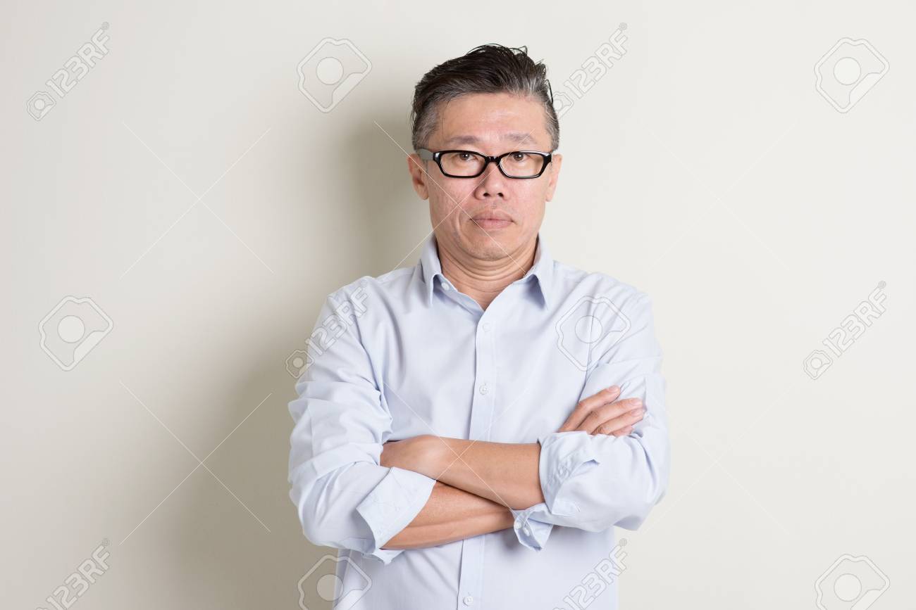 Portrait of single mature 50s Asian man in casual business arms crossed and standing over plain background with shadow. - 51835747 Portrait of single mature 50s Asian man in casual business arms crossed and standing over plain background with shadow. - 51835747