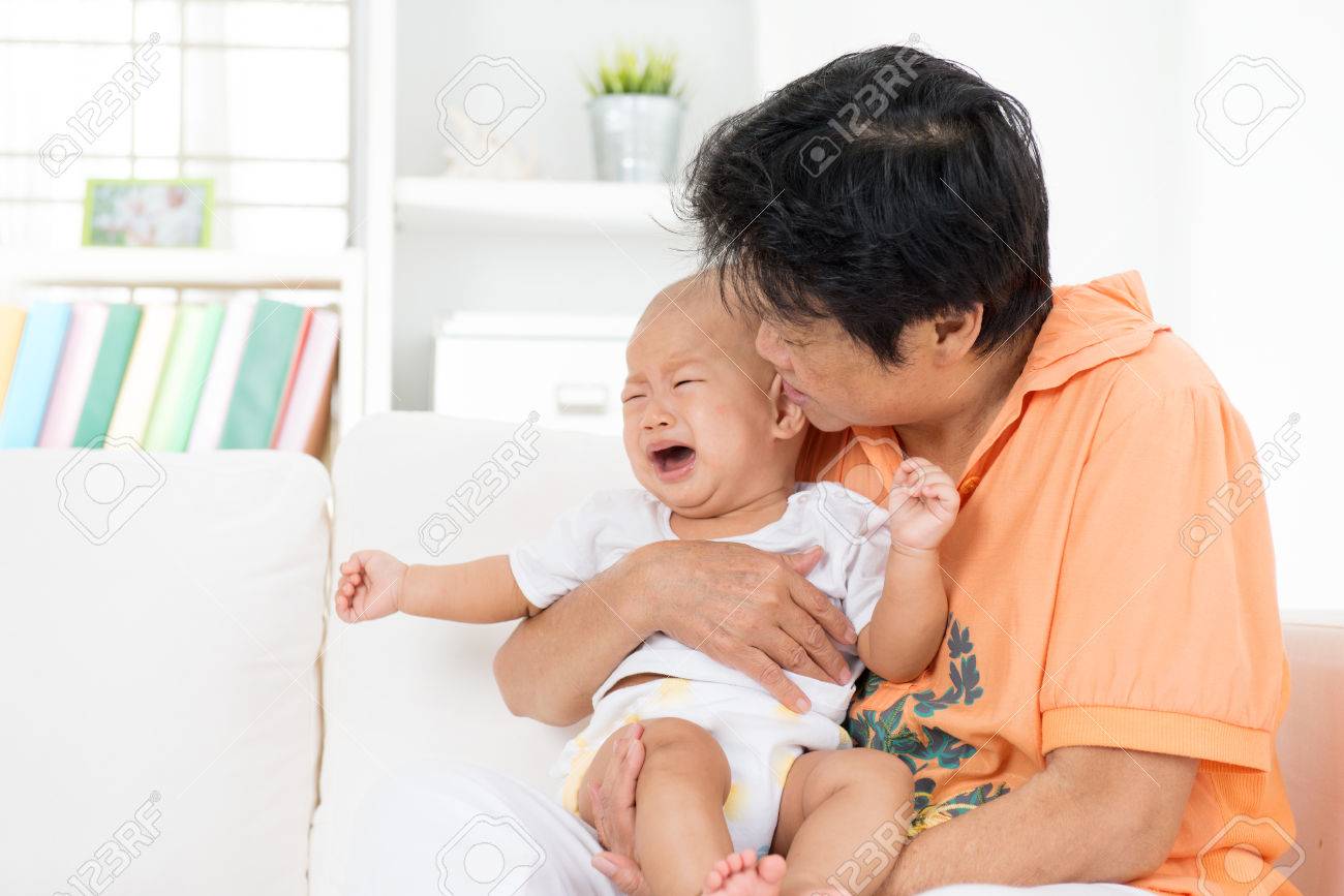 Babysitter comforting crying baby boy at home. - 52943997 Babysitter comforting crying baby boy at home. - 52943997