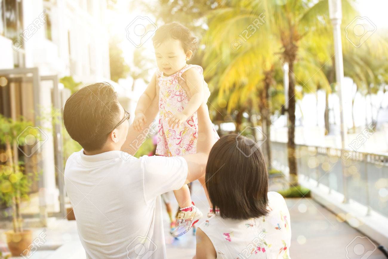 Rear view of Asian family enjoying outdoor activity together, playing with kid in beautiful sunset during holiday vacation, outside the resort. - 70563409 Rear view of Asian family enjoying outdoor activity together, playing with kid in beautiful sunset during holiday vacation, outside the resort. - 70563409