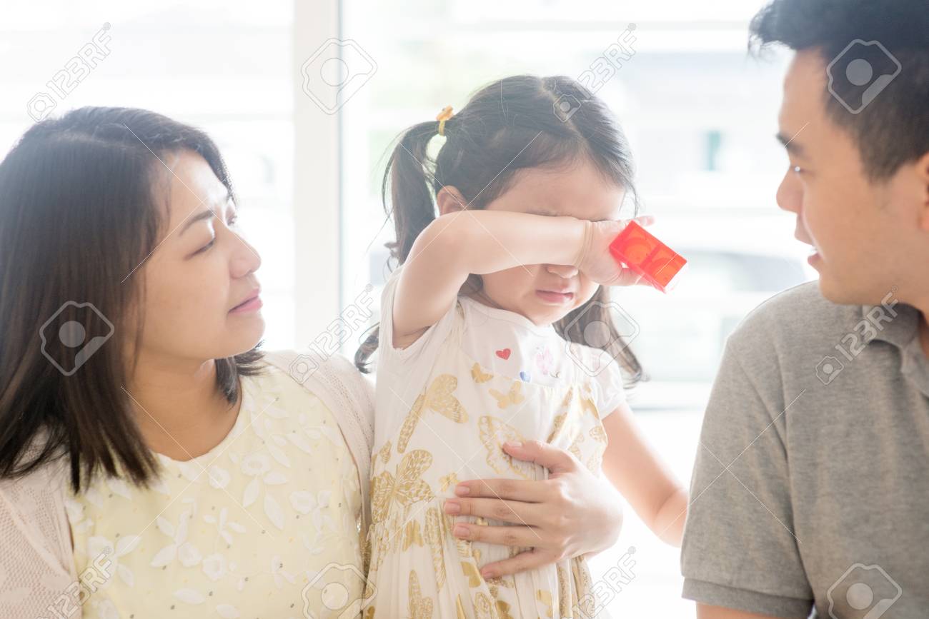 Parents comforting crying daughter. Asian family at home, natural living lifestyle indoors. - 96889850 Parents comforting crying daughter. Asian family at home, natural living lifestyle indoors. - 96889850