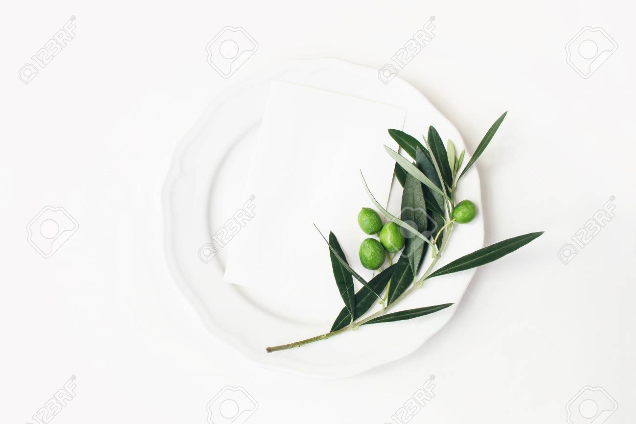 Festive table summer setting with olive leaves, branch and fruit on porcelain plate. Blank paper card mockup scene. Mediterranean wedding or restaurant menu concept. Flat lay, top view. - 117352090 Festive table summer setting with olive leaves, branch and fruit on porcelain plate. Blank paper card mockup scene. Mediterranean wedding or restaurant menu concept. Flat lay, top view. - 117352090