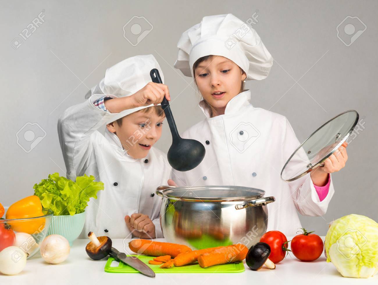cooking little boy and girl looking in pan on table with vegetables - 61380381 cooking little boy and girl looking in pan on table with vegetables - 61380381
