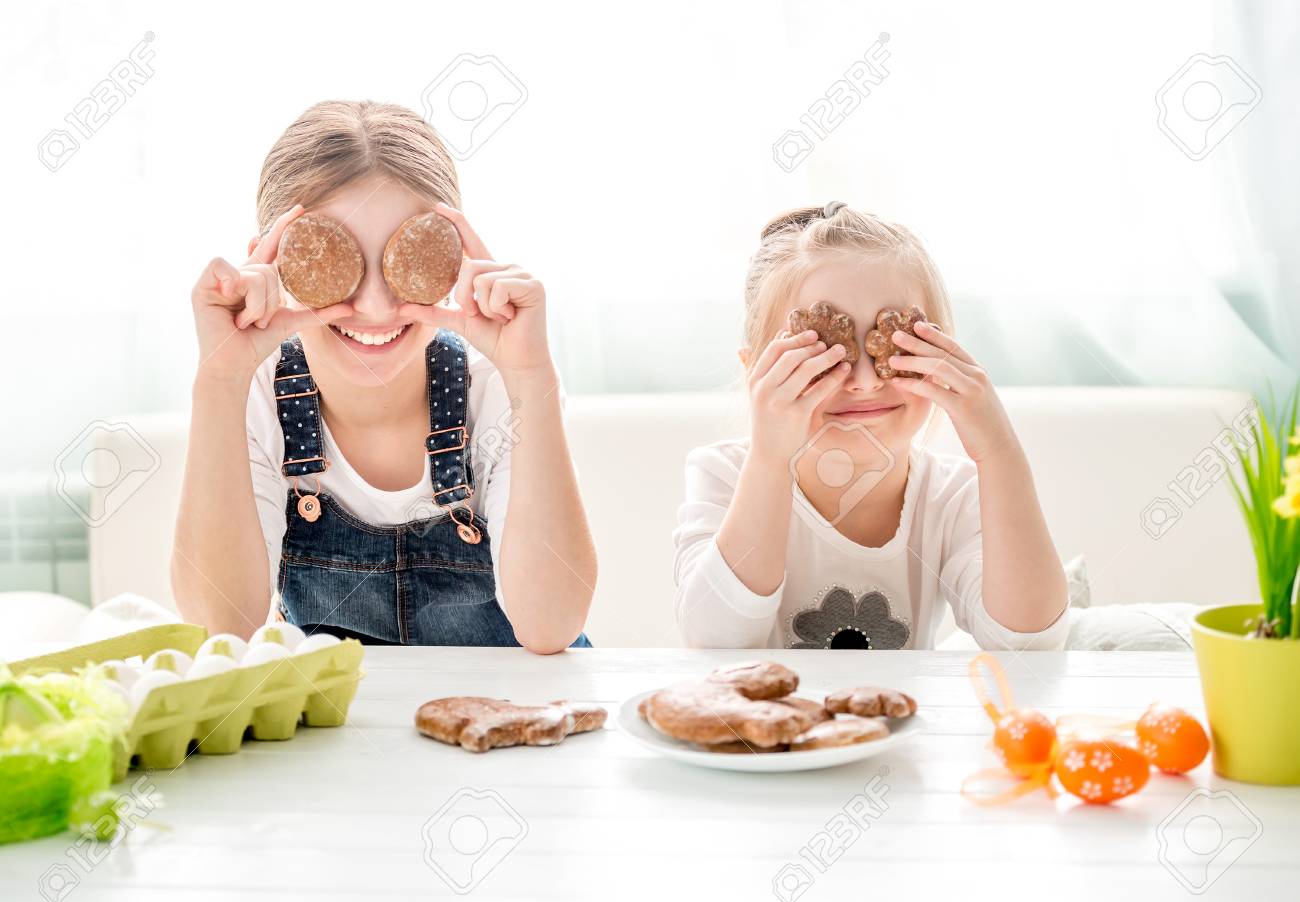 Happy little girls holding Easter cookies in front of their eyes - 102331459 Happy little girls holding Easter cookies in front of their eyes - 102331459