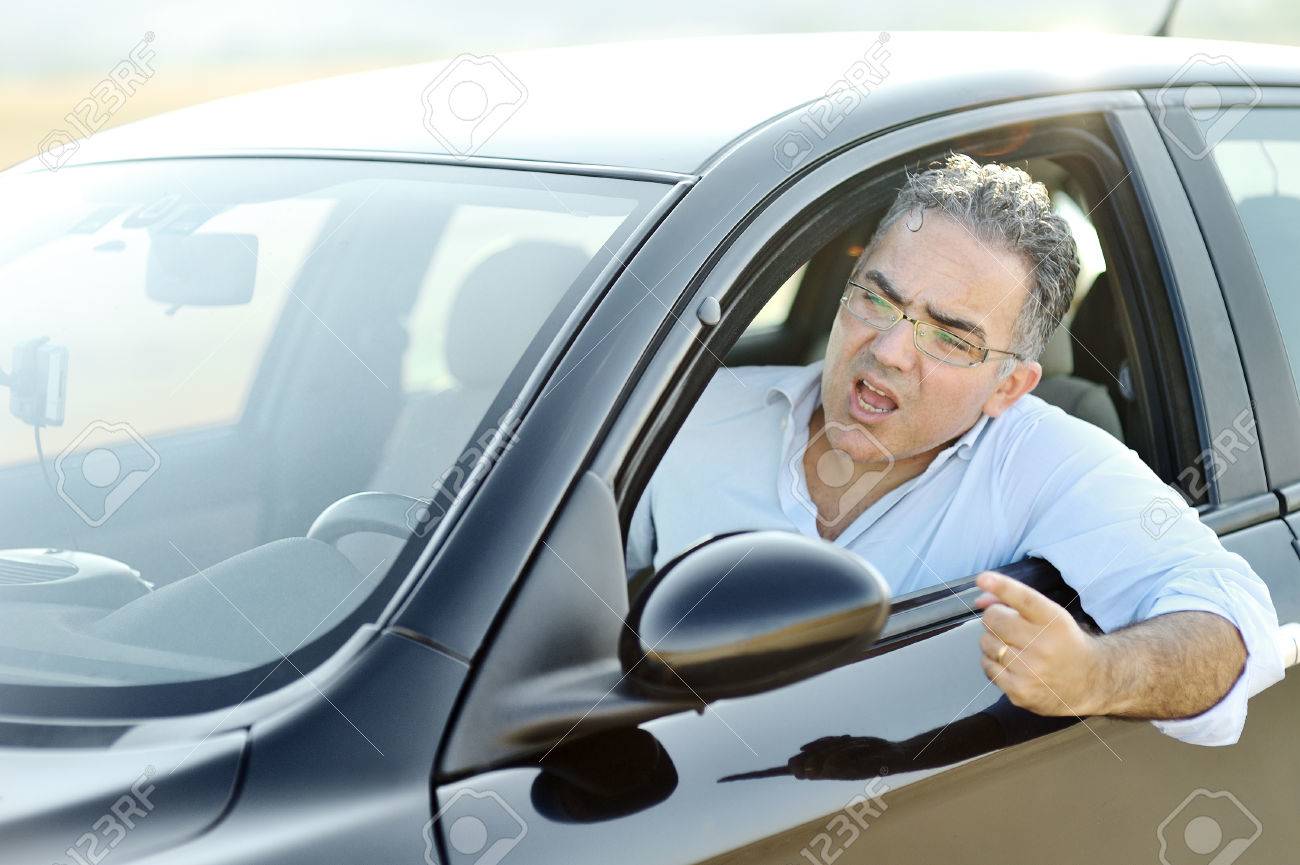 Road rage concept - irritated man screams and gestures while driving a black car - 78861577 Road rage concept - irritated man screams and gestures while driving a black car - 78861577