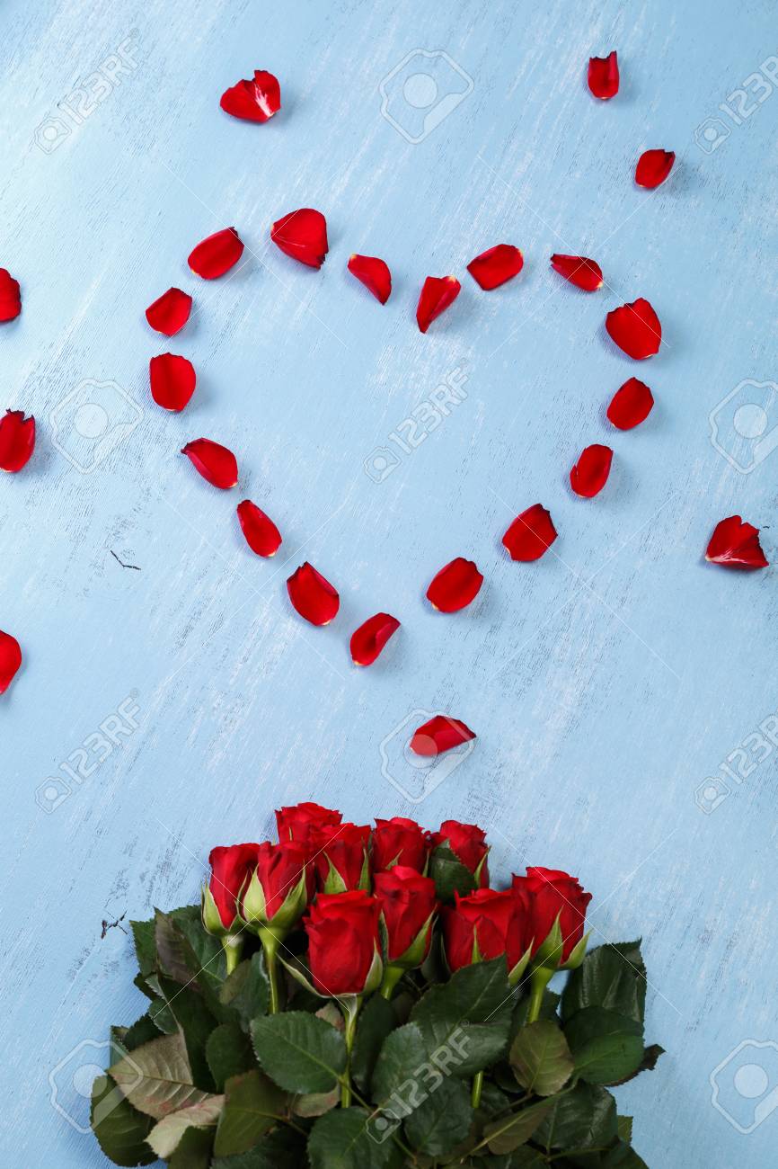 heart of red rose petals on blue painted rustic background