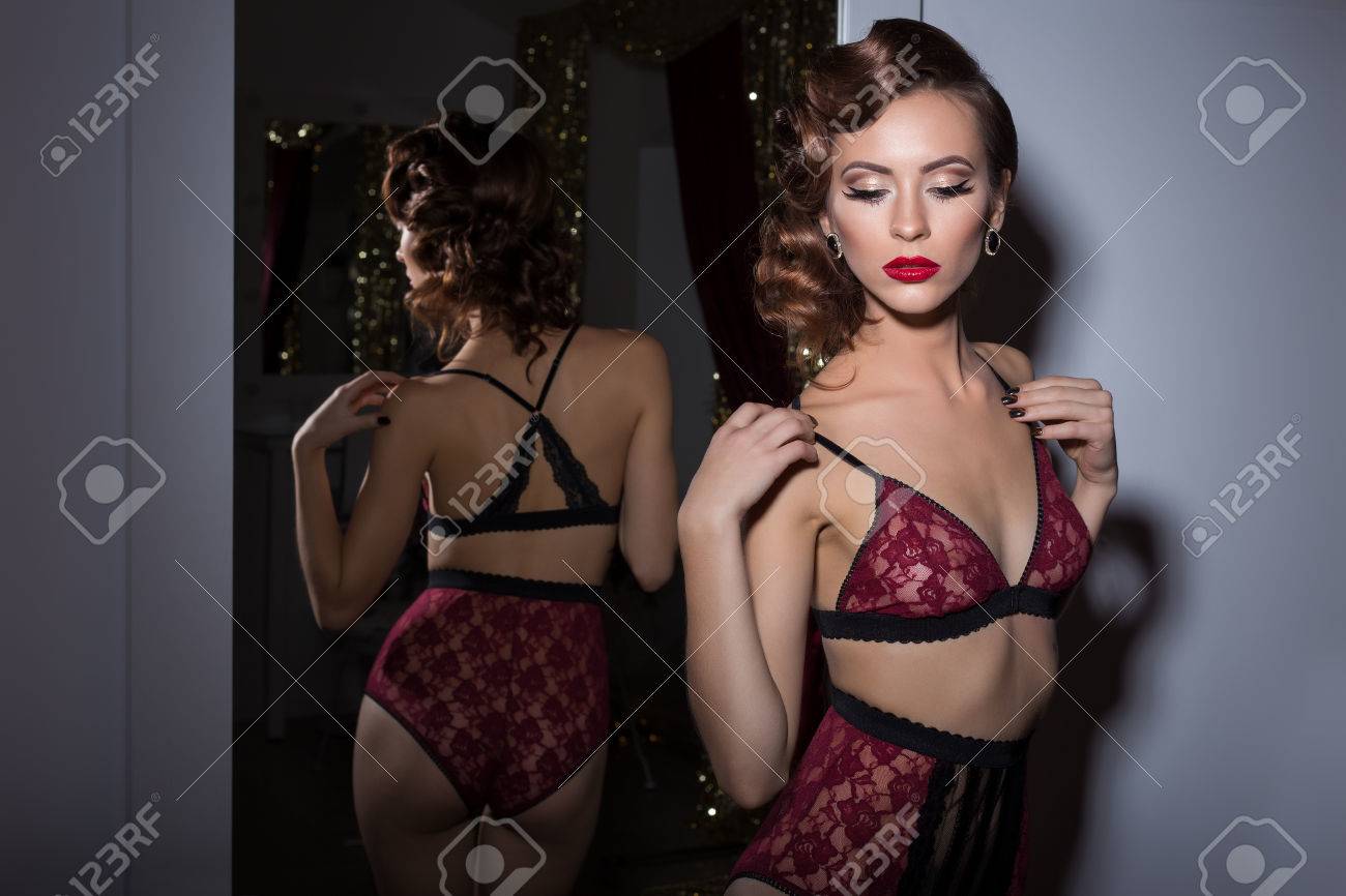 Hermosa Mujer En Ropa Interior De Encaje Delicado Años 20 De Retro Con Elegante Cabello Y Maquillaje De Noche Se Encuentra Cerca Del Espejo En El La Habitación Fotos,