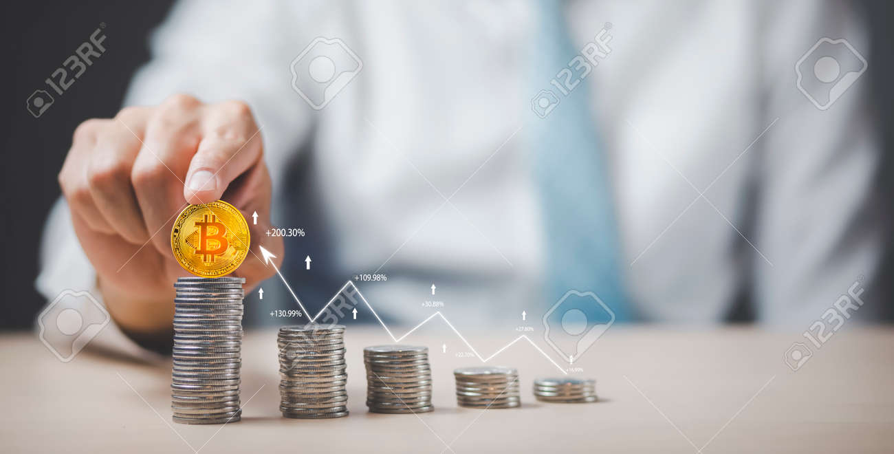 사업가는 나무 테이블에 동전 더미에 비트코인을 들고 외환 차트 배경에 황금 비트코인 사다리를 사용하여 아이디어와 투자 예산 시장 금융  성장 개념을 절약합니다. 로열티 무료 사진, 그림, 이미지 그리고 스톡포토그래피. Image 172404017