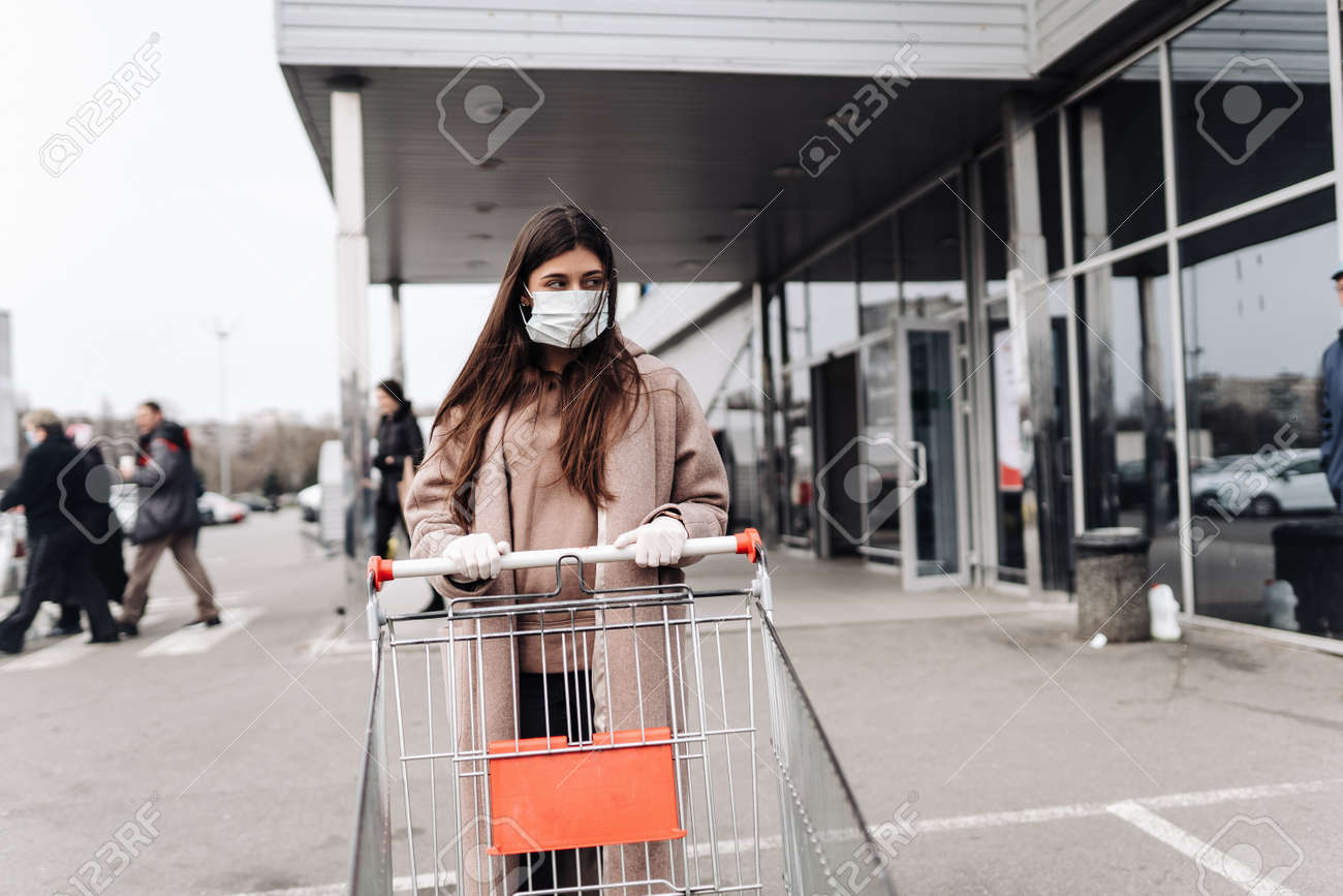 Young woman wearing protection face mask against coronavirus 2019-nCoV pushing a shopping cart. - 144659950 Young woman wearing protection face mask against coronavirus 2019-nCoV pushing a shopping cart. - 144659950