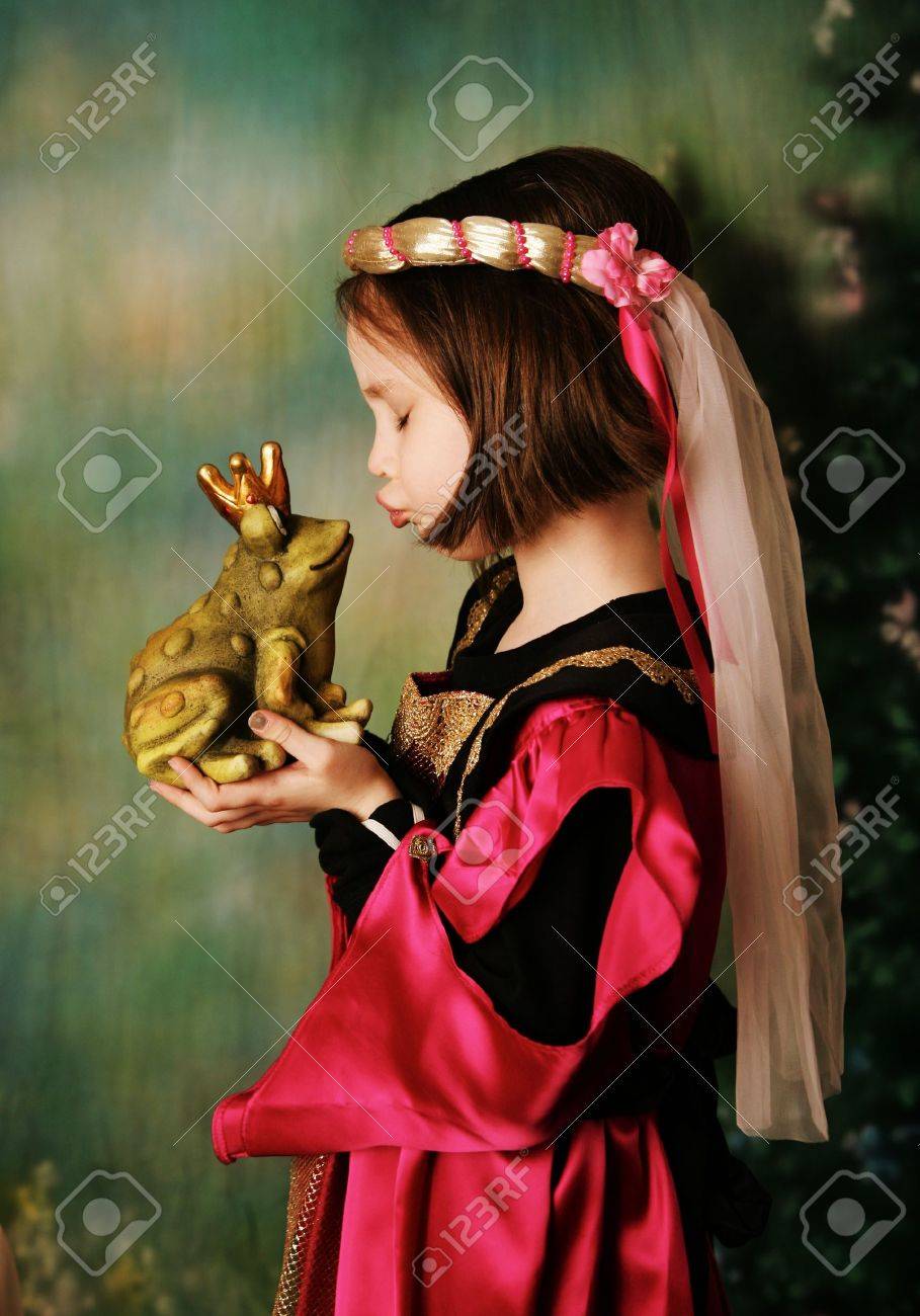 Portrait of a cute young preschool girl dressed as a princess in a pink and gold gown, posing and kissing a frog prince wearing a crown - 8710221 Portrait of a cute young preschool girl dressed as a princess in a pink and gold gown, posing and kissing a frog prince wearing a crown - 8710221