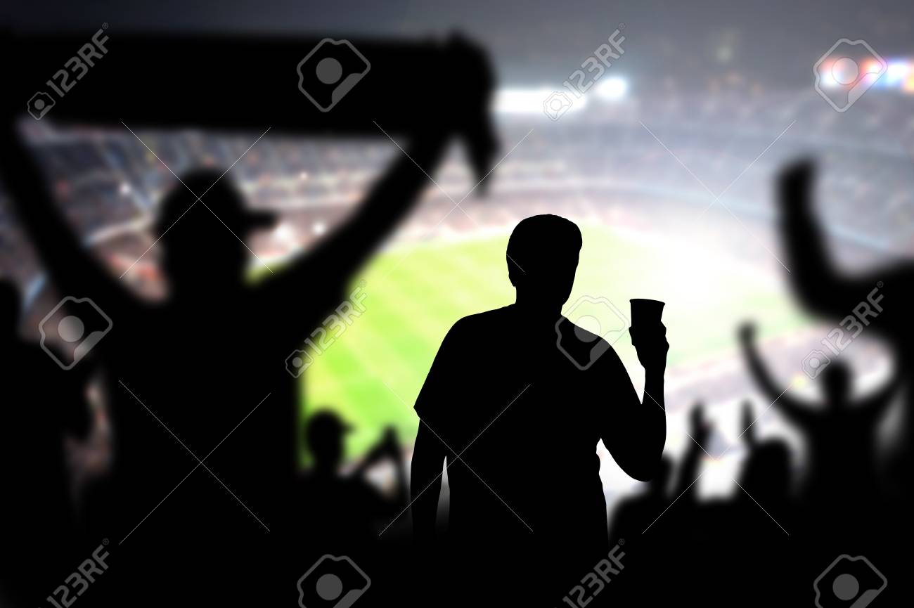 Football Fan Drinking Beer In Crowd In Stadium. Man With Alcohol Beverage  In Soccer Audience At A Game. Holding Pint. Drunk Person In Live Sport  Event. Silhouette People Watching Match In Arena., image size:1300x865