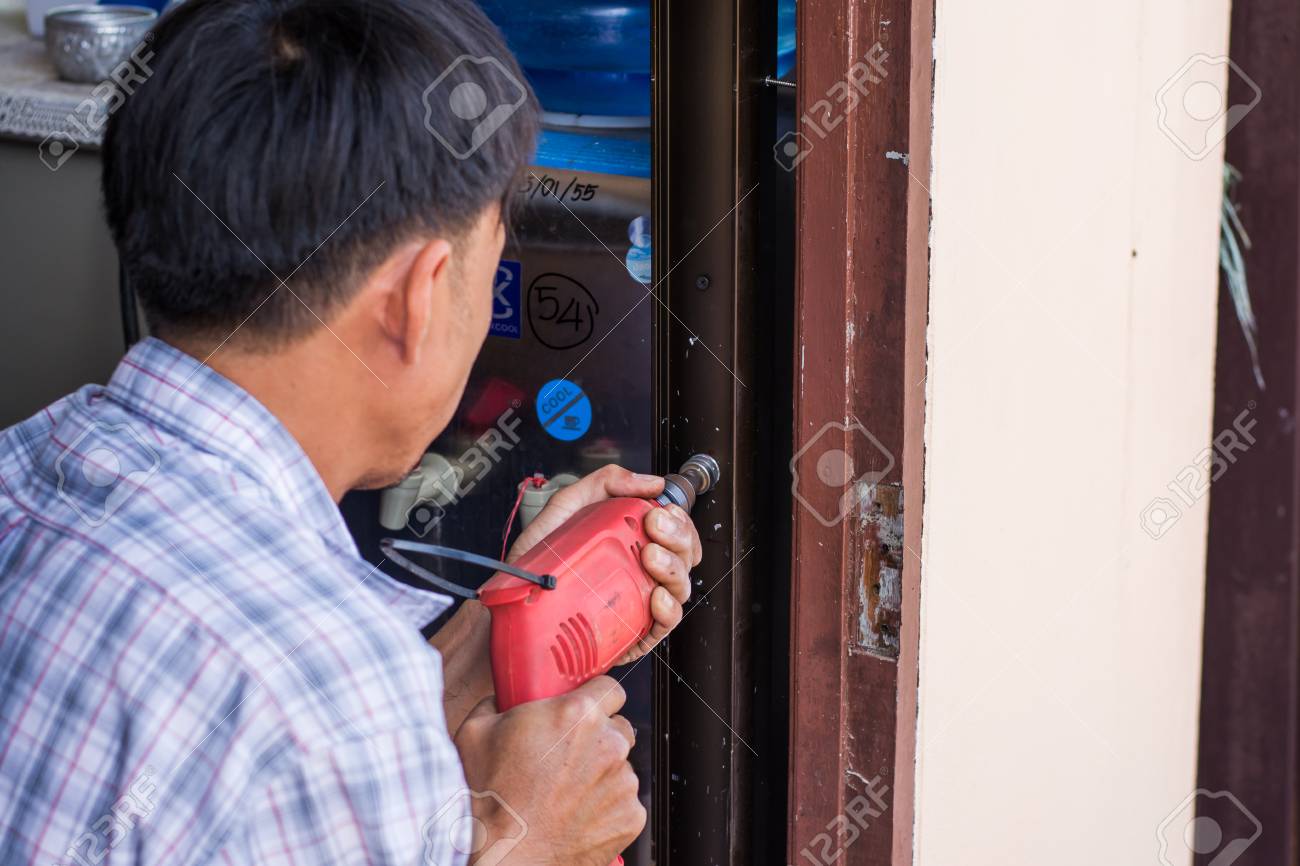 Carpenter At Lock Installation With Electric Drill Into Interior