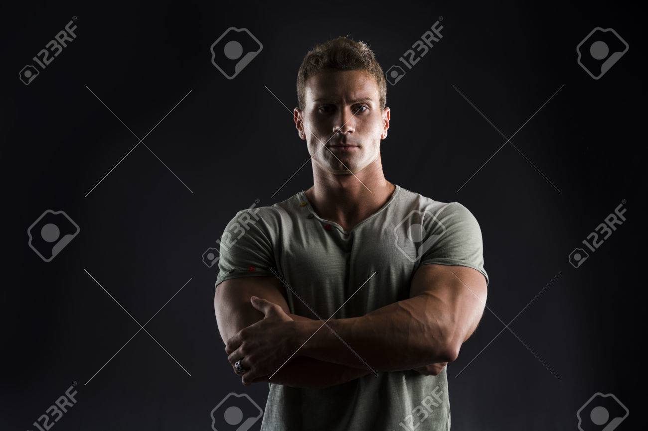 腕を組んで彼の胸にカメラを見て暗い背景にハンサムな筋肉フィット若い男 の写真素材 画像素材 Image