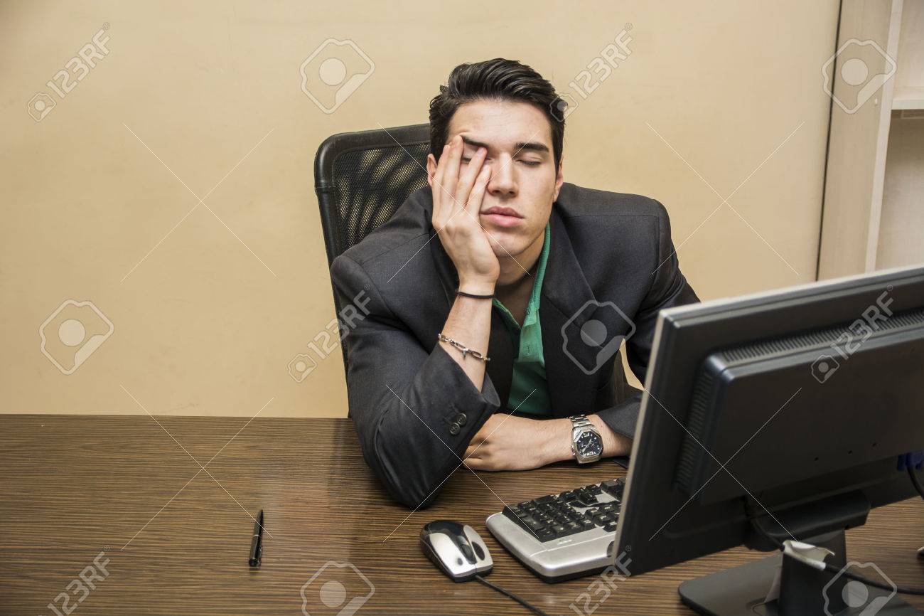 tired bored young businessman sitting at his desk in front of